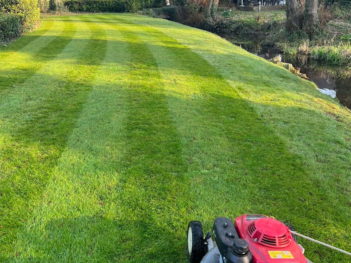 Freshly striped lawn beside a river with a mower in the corner